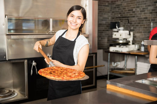 Pizzaiola sorridente in pizzeria moderna con forno a legna mentre sforna una pizza appena cotta, ambiente professionale