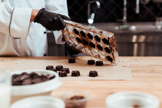 Maestro cioccolatiere versa cioccolatini temperati da stampo su carta forno, laboratorio professionale, dettaglio lavorazione