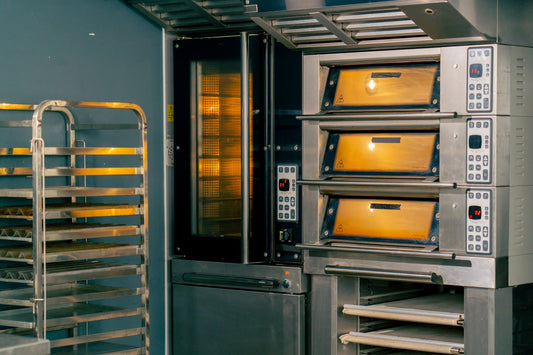 Forno professionale acceso in cucina attrezzata, teglie in acciaio inox e pannelli di controllo digitali, ambiente pulito