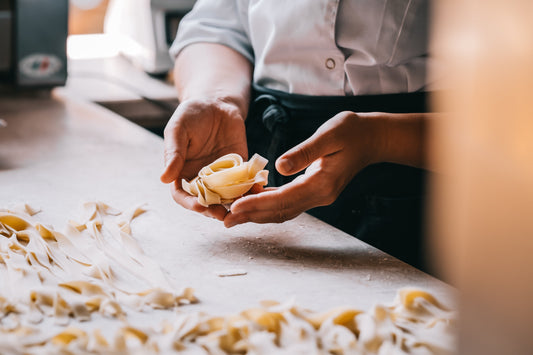 Chef prepara tagliatelle fresche fatte a mano su banco da lavoro, dettaglio mani e pasta artigianale, laboratorio ristorante